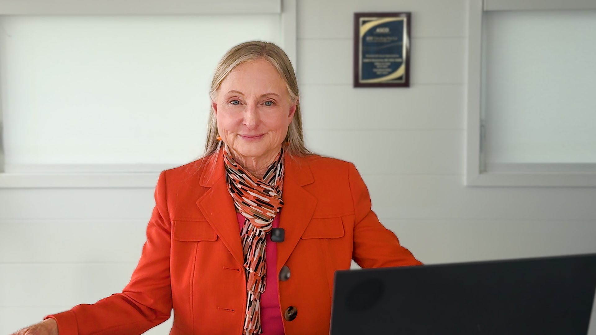 Dr. Linda Bosserman smiling, in an orange jacket and patterned scarf